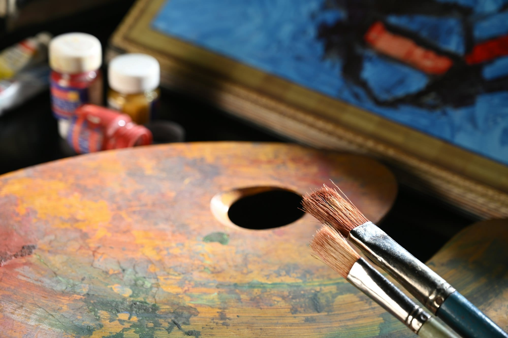 Une palette de peintre en bois couverte de couleurs, avec deux pinceaux et des pots de peinture.