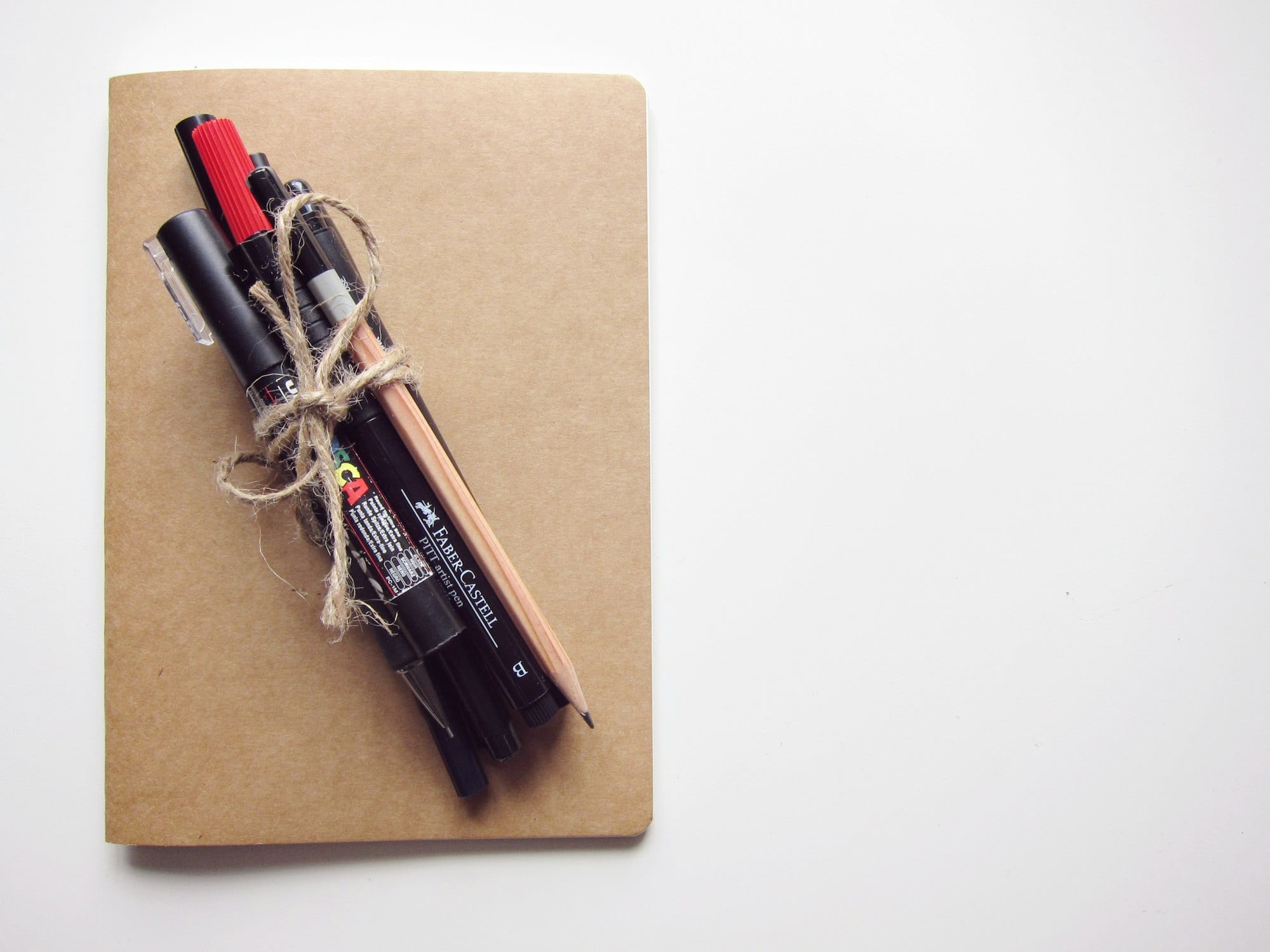 Un carnet à couverture kraft avec des feutres et un crayon noués par une ficelle.